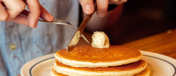 pancakes en un plato y persona cortándolo para comer